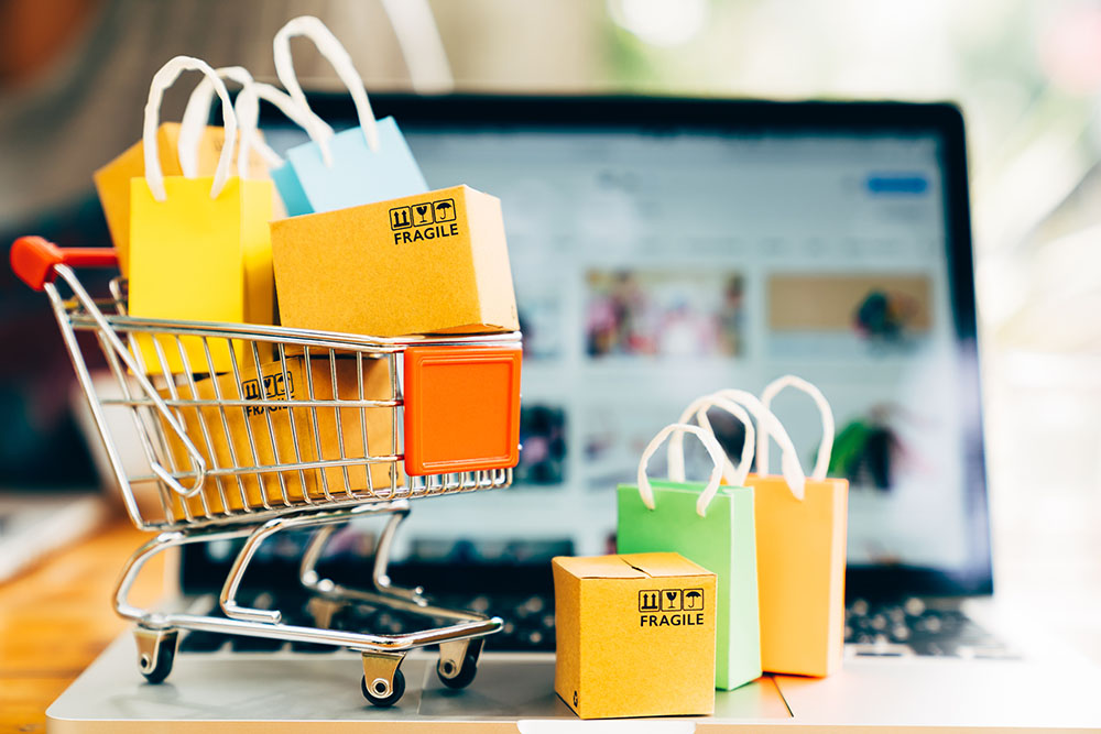 tiny product packages and shopping bags in a tiny cart sitting on a laptop open on a shopping page